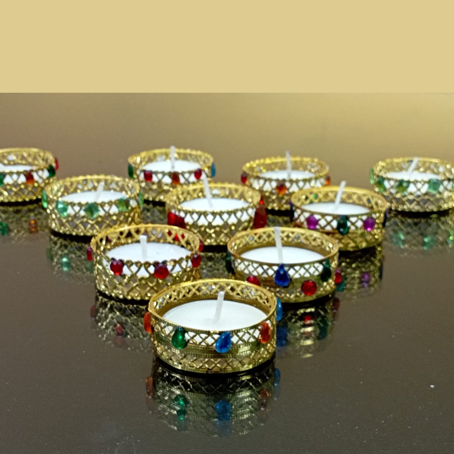 Decorative candles in gold holders with colorful beads on a reflective surface.