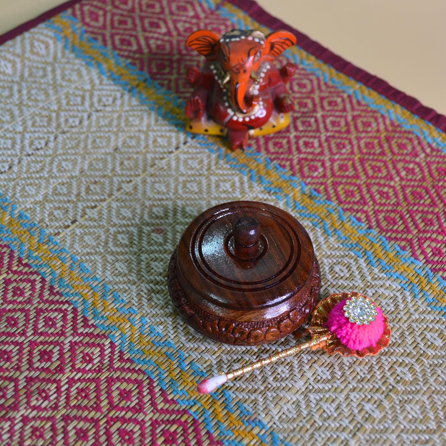 Decorative wooden item with a pink and gold ornament on a patterned fabric background