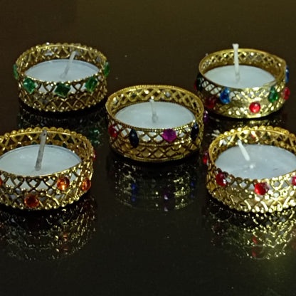 Set of five decorative candles in gold holders with gemstones on a reflective surface.