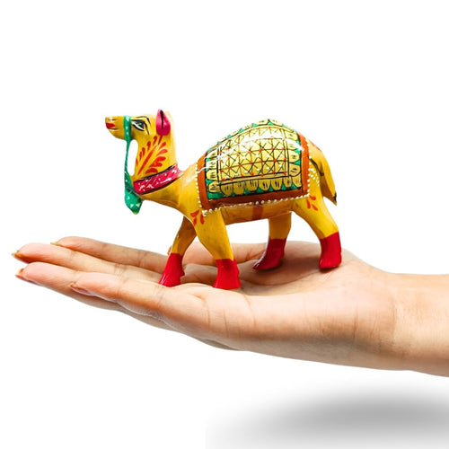A small hand-painted camel figurine with yellow, green, red, and orange details, displayed on a person's open palm against a white background.