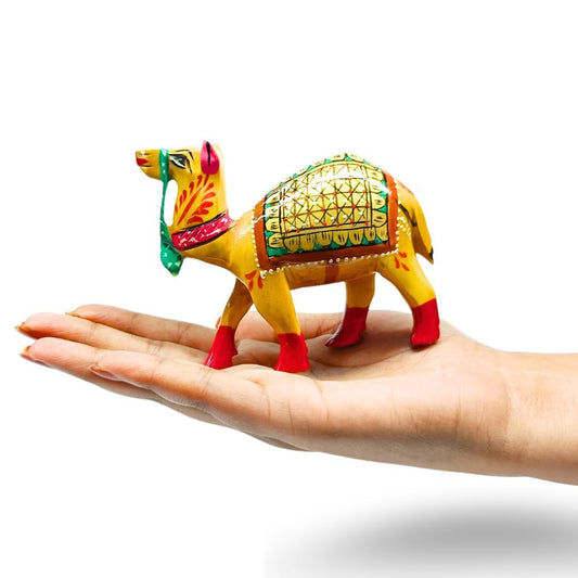 A small hand-painted camel figurine with yellow, green, red, and orange details, displayed on a person's open palm against a white background.