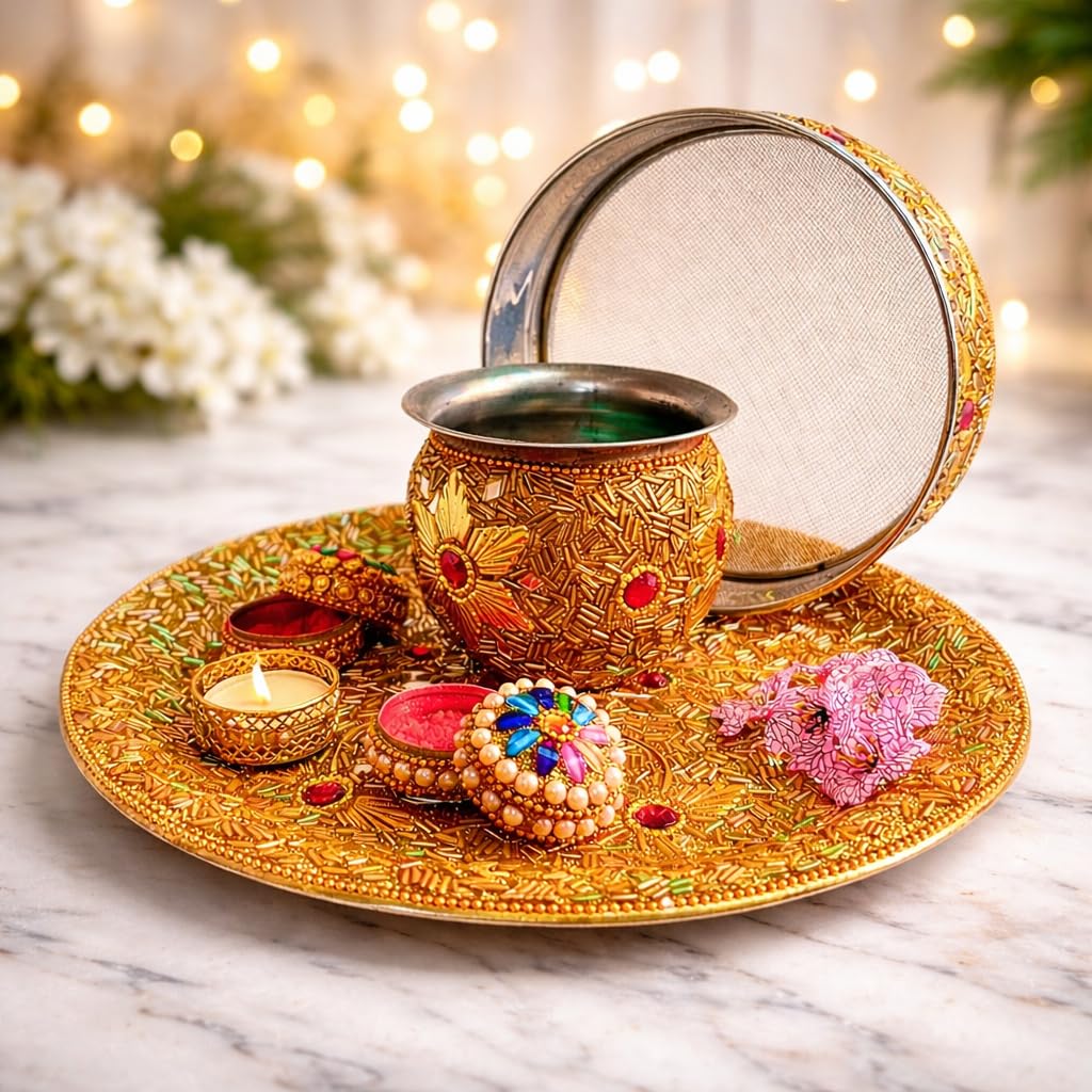 An ornate gold-toned Diwali decoration set on a marble surface, featuring a decorative pot with a lid, a round tray, a lit candle, a colorful ornament, and pink flowers, with warm blurred lights in the background.