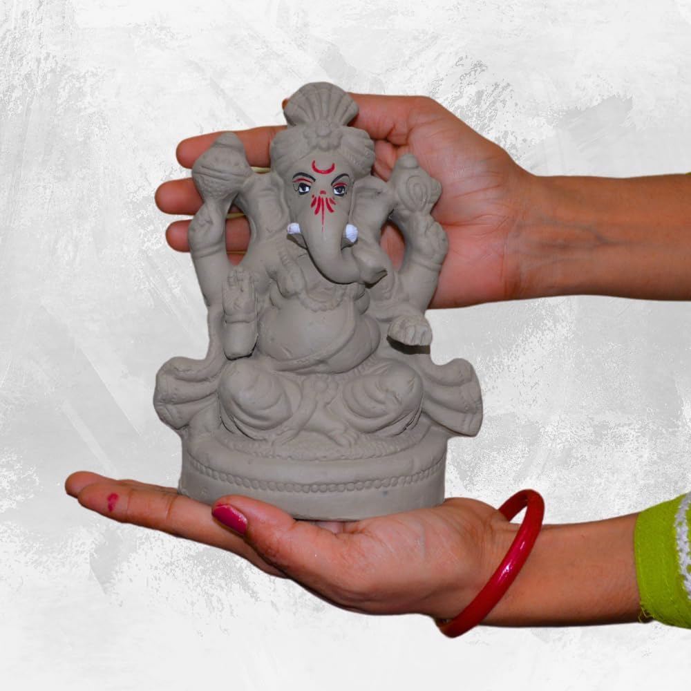 A small gray clay Ganesha statue being held in two hands against a light textured background.