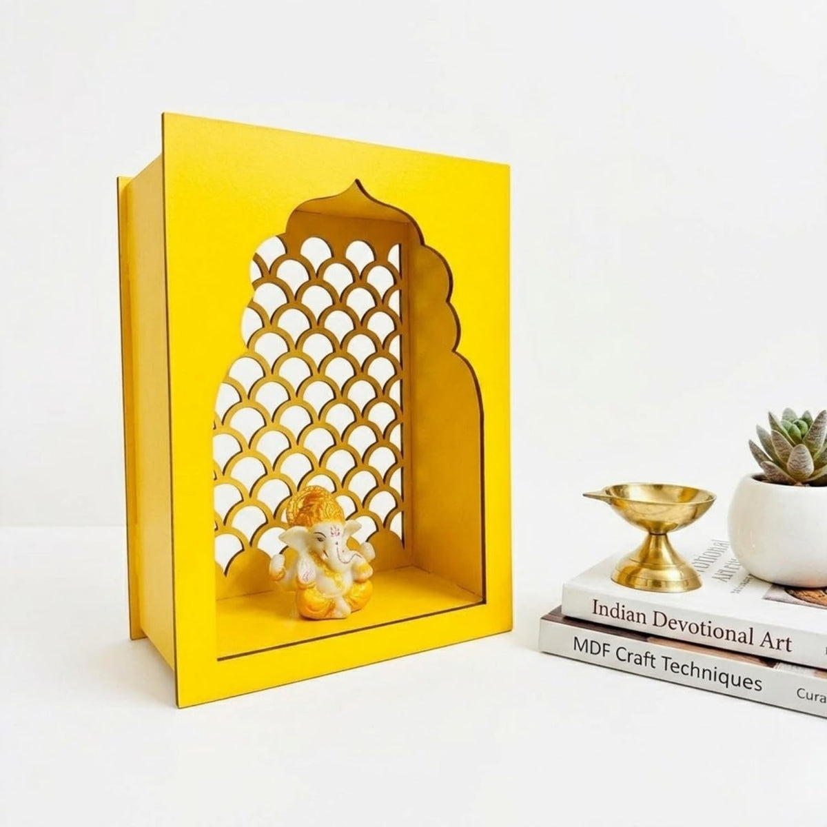 A bright yellow MDF decorative box with an arched cutout featuring a scalloped pattern, styled on a white surface next to books, a small brass lamp, and a potted succulent.