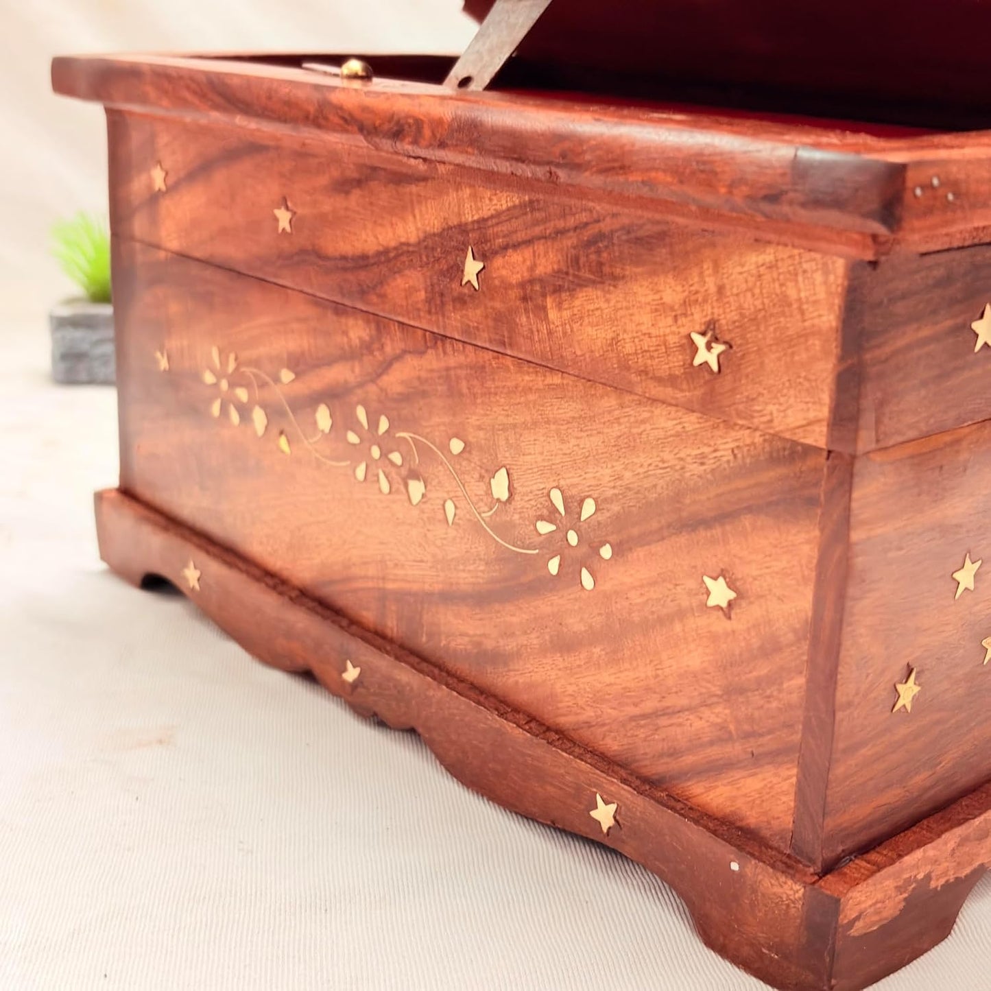 A close-up of a reddish-brown wooden chest or box with brass star inlays and delicate floral inlay details on the front, shown on a light neutral surface.