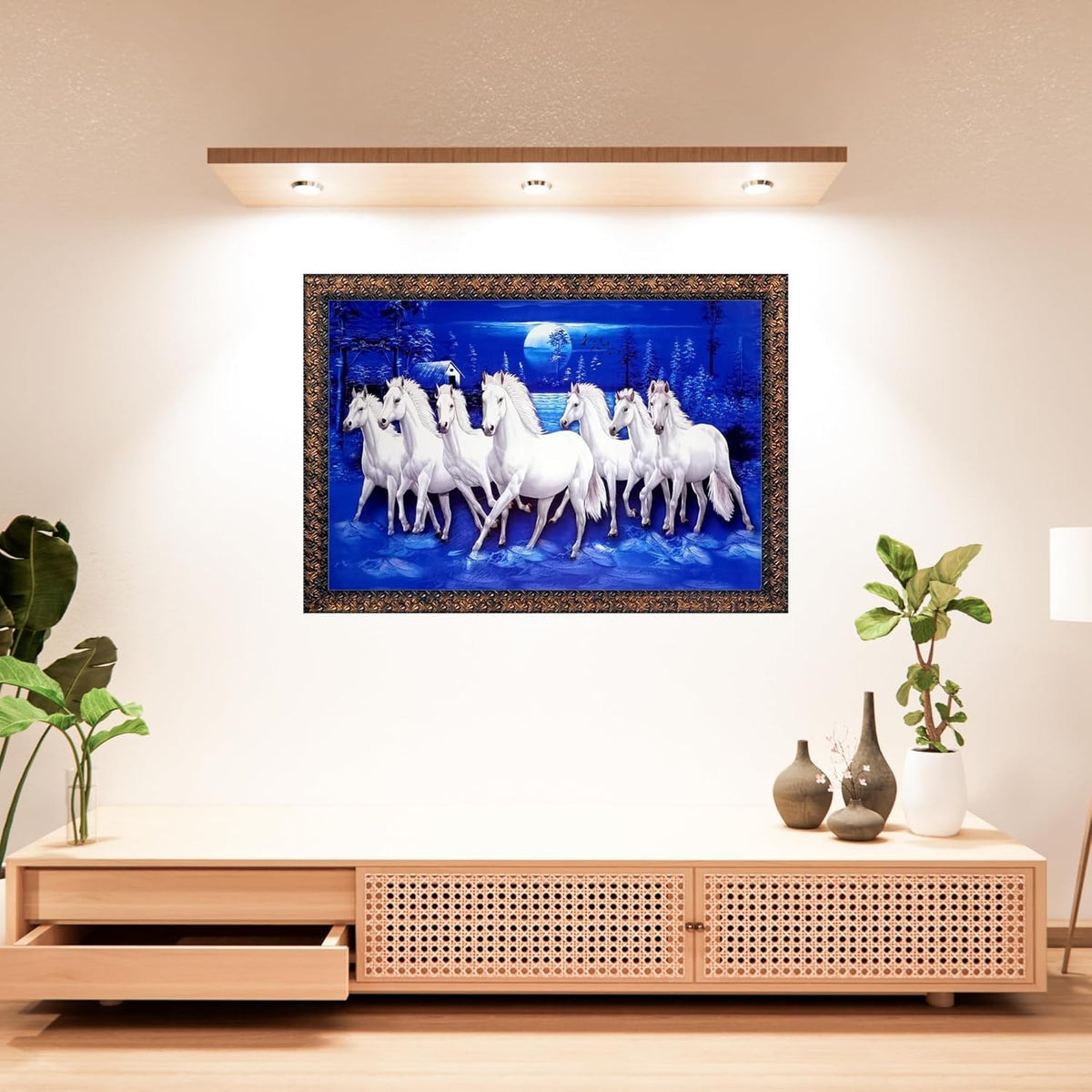 A framed wall art piece showing a group of white horses under a blue night sky, displayed above a light wood media console in a styled interior room.