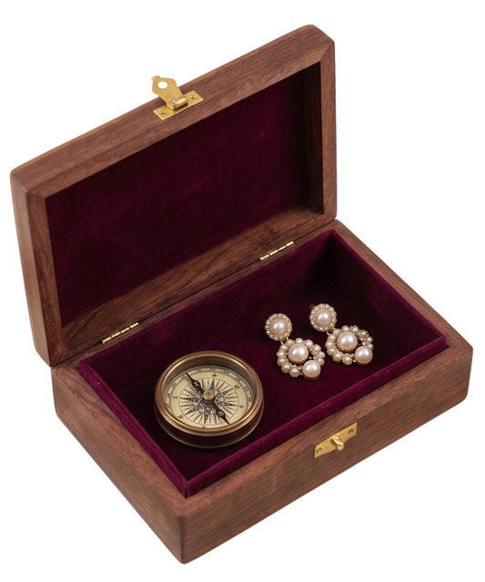 An open wooden presentation box with a deep burgundy velvet interior, holding a small round brass compass and a pair of pearl-and-gold earrings, shown on a white background.