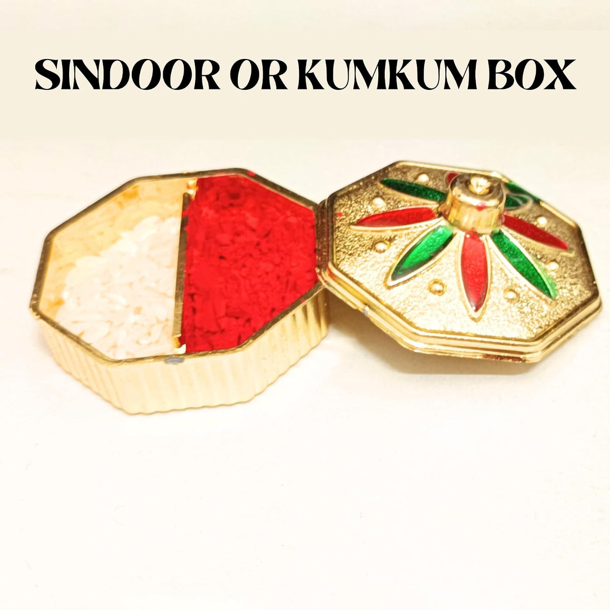 An octagonal gold-toned kumkum box shown open on a white background, with one half filled with white powder and the other filled with red powder. The lid is visible and decorated with red and green floral details.