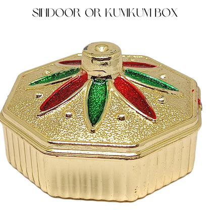 A gold-colored octagonal box with a textured lid, featuring red and green glittery petal designs on top. The text 'SHIDOOR OR KUMIKUM BOX' is written at the top of the image on a white background.