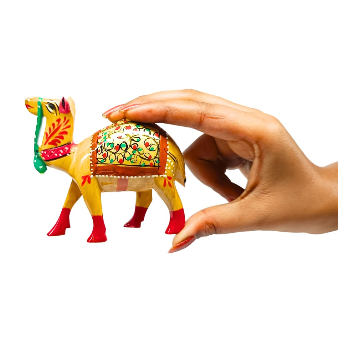 A small hand-painted camel figurine with a yellow body, red hooves, and a decorated saddle, being held by a person's hand against a white background.