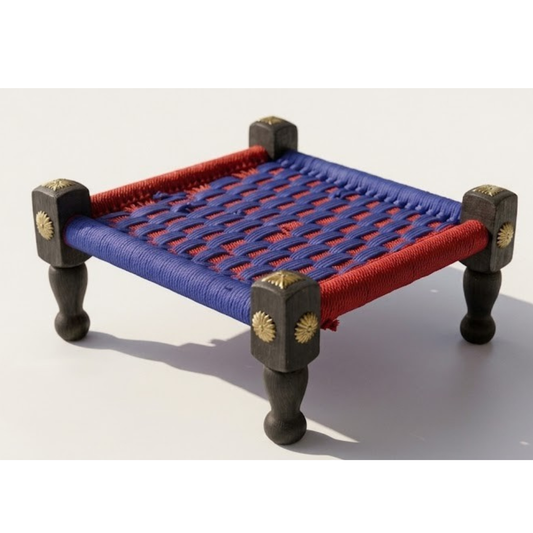 A traditional Indian wooden charpai cot with a woven red and blue rope bed, supported by four dark wooden legs with brass star-shaped decorative accents.