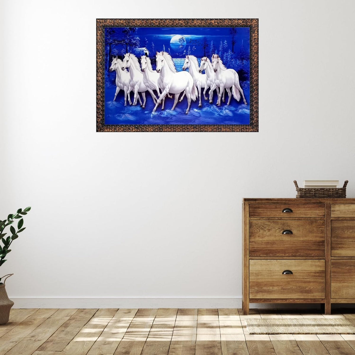 A framed wall art print depicting a group of white horses under a full moon in a blue night scene, displayed on a white wall above a wooden dresser in a styled room.