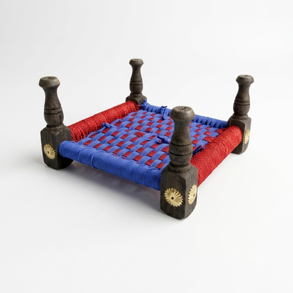 A traditional Indian charpai woven chair with a blue and red woven cord seat supported by four dark brown wooden legs with gold sun motifs, shown on a white background.
