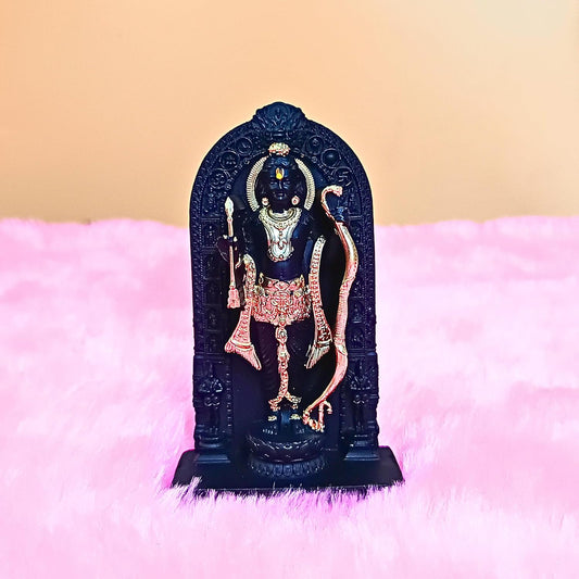 A small black Hindu deity statue, likely Lord Shiva, adorned with gold and pink gemstone-like details, standing on a pink fluffy surface against a beige background.