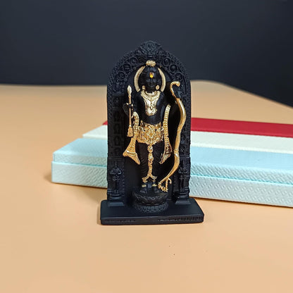 A small black and gold Lord Hanuman statue standing in front of stacked light blue and red boxes on a beige surface.