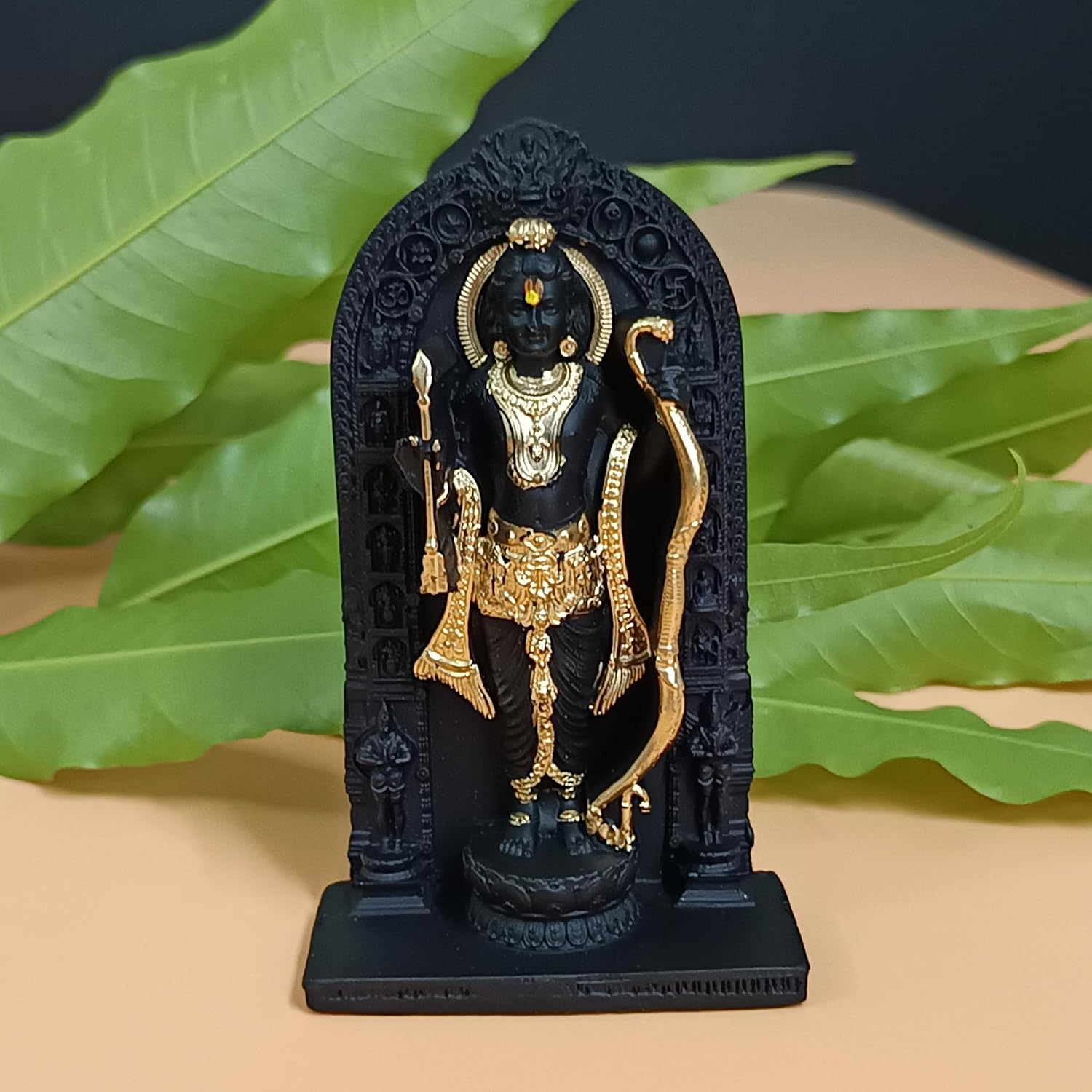 A small black and gold Lord Shiva statue displayed on a beige surface with green leaves in the background.