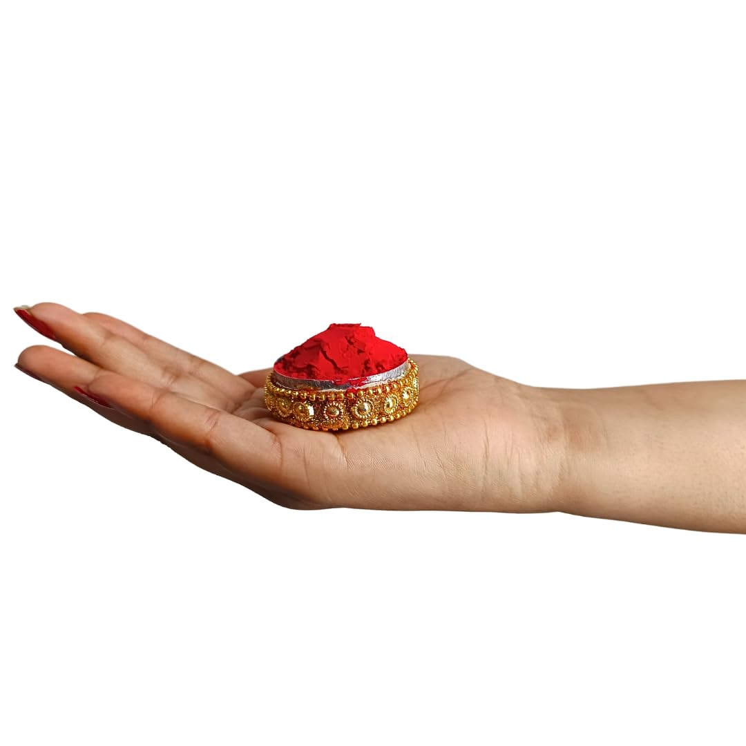A hand holding a small decorative gold container filled with bright red powder, shown against a plain white background.