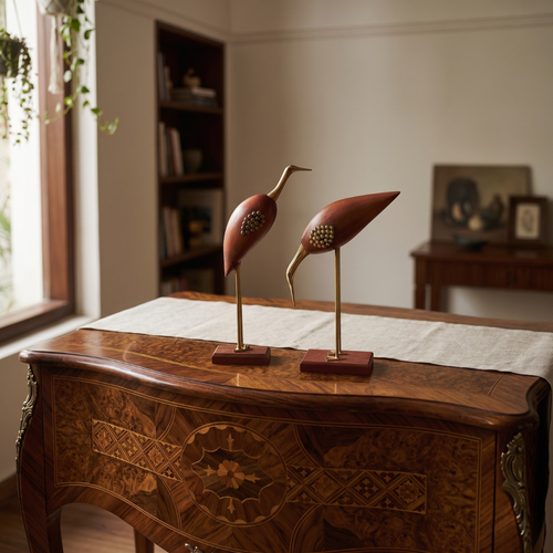 Two decorative wooden bird sculptures with gold-toned metal legs and reddish-brown bases, displayed on a wooden console table in a softly lit room.